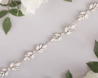 May include: A silver and white crystal bridal belt with a delicate floral design. The belt is made of small, oval-shaped crystals that are arranged in a repeating pattern.