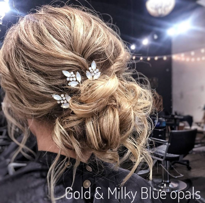 May include: A woman with blonde hair styled in a messy bun with three gold hair clips with milky blue opals. The hair clips are in the shape of leaves. The text "Gold & Milky Blue opals" is at the bottom of the image.