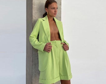 May include: A lime green blazer and matching shorts set. The blazer has a notched lapel and a single button closure. The shorts have a high waist and pleats in the front.