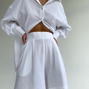 Pode incluir: Uma camisa branca de linho com mangas compridas e um par de cal&ccedil;&otilde;es brancos de linho. A camisa est&aacute; desabotoada e amarrada na cintura.