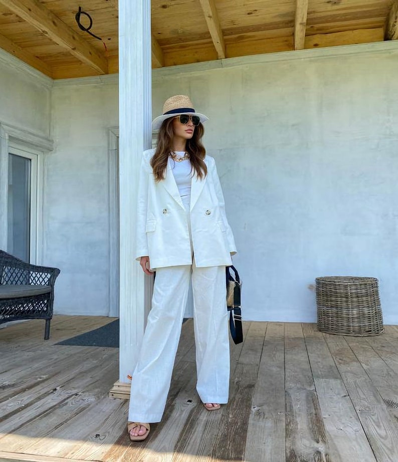 May include: A white linen blazer and wide-leg pants set with a straw hat and sunglasses. The outfit is a classic summer look.