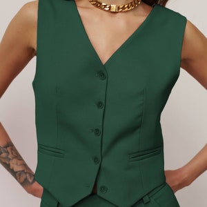 May include: A dark green sleeveless waistcoat with a V-neckline and a row of buttons down the front. The waistcoat has two pockets on the front and is made of a smooth fabric.