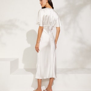 May include: A white satin midi dress with a V-neckline and short sleeves. The dress has a fitted bodice and a flowing skirt.