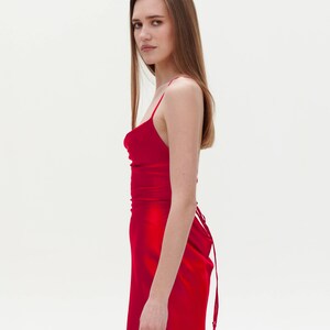 Puede incluir: Una mujer con un vestido de sat&eacute;n rojo con cuello de pico y un lazo en la espalda.