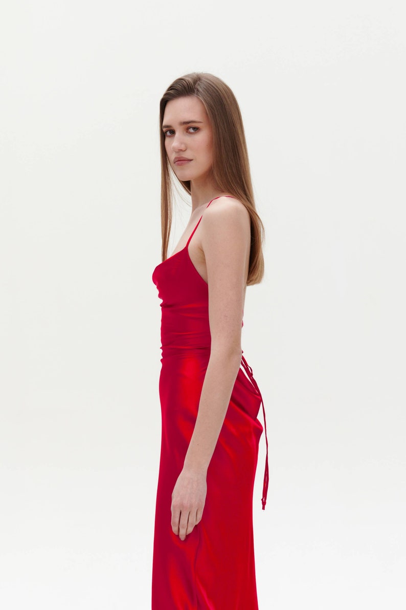 Puede incluir: Una mujer con un vestido de sat&eacute;n rojo con cuello de pico y un lazo en la espalda.