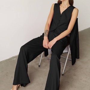 Pode incluir: Uma mulher vestindo um top preto sem mangas e cal&ccedil;as largas senta-se em uma cadeira de metal. Ela est&aacute; usando &oacute;culos de sol pretos e tem uma tatuagem no bra&ccedil;o.
