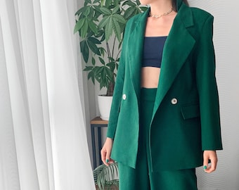May include: A green double-breasted blazer with a matching pair of pants. The blazer has two buttons and a pocket on the left side.