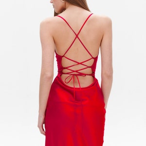 Puede incluir: Un vestido midi de sat&eacute;n rojo con un detalle de encaje en la espalda. El vestido tiene un corpi&ntilde;o ajustado y una falda fluida.