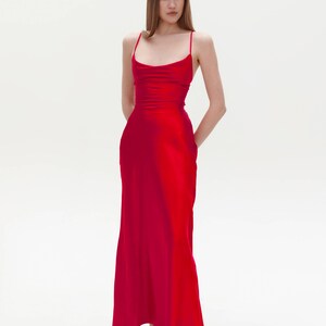 Puede incluir: Una mujer con un vestido largo de sat&eacute;n rojo con cuello de pico y tirantes finos. Est&aacute; de pie sobre un fondo blanco.