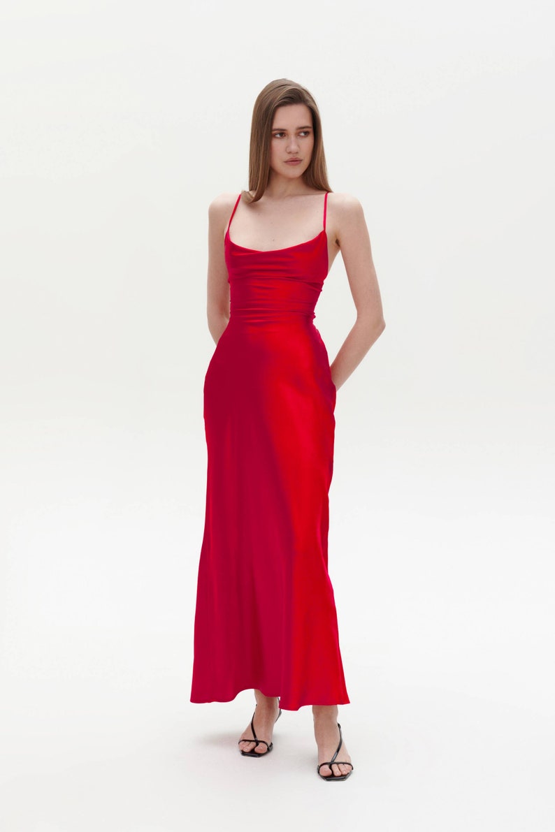Puede incluir: Una mujer con un vestido largo de sat&eacute;n rojo con cuello de pico y tirantes finos. Est&aacute; de pie sobre un fondo blanco.
