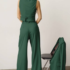 May include: A green sleeveless waistcoat and wide-leg trousers set. The waistcoat has a belt and the trousers have a high waist. A matching green blazer is draped over a chair.