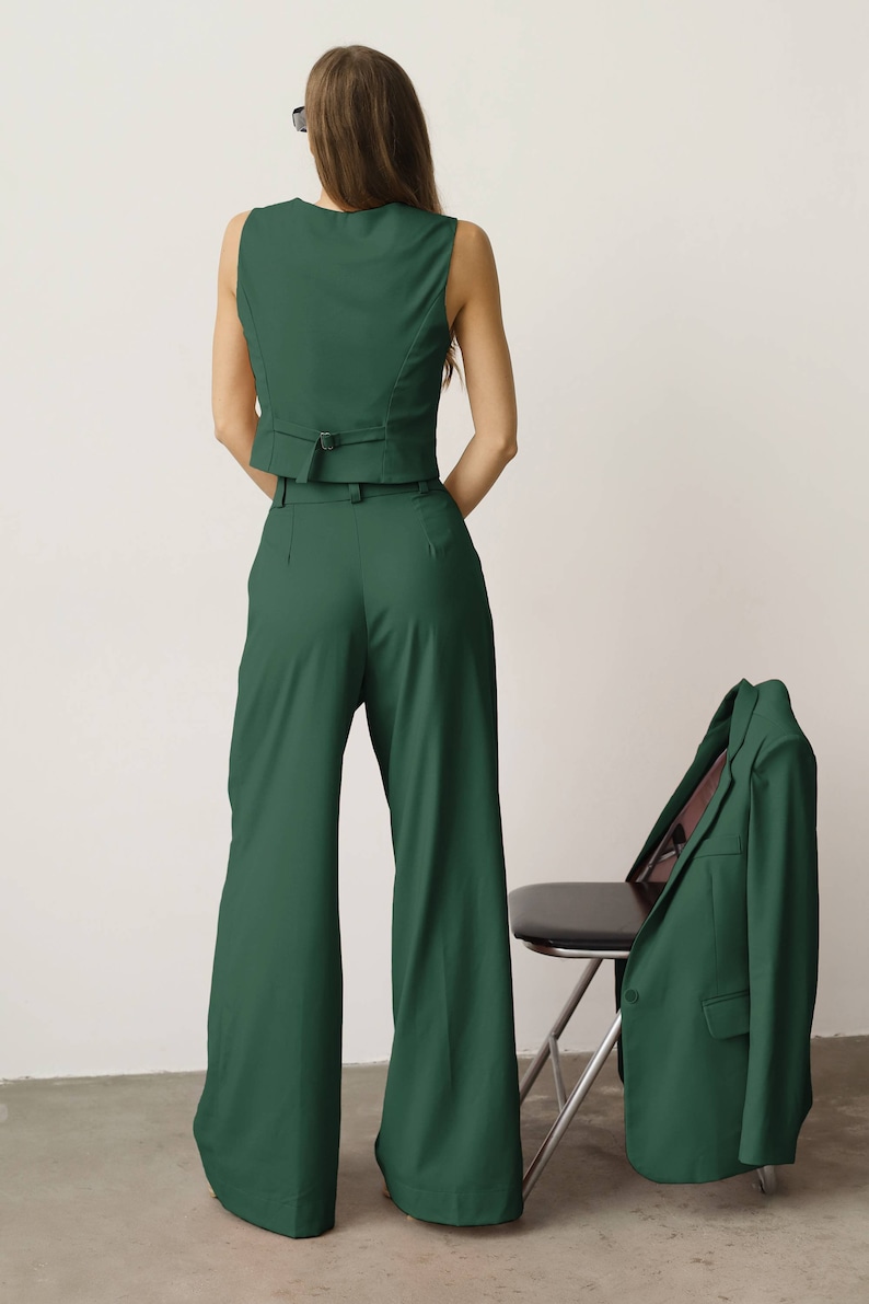 May include: A green sleeveless waistcoat and wide-leg trousers set. The waistcoat has a belt and the trousers have a high waist. A matching green blazer is draped over a chair.