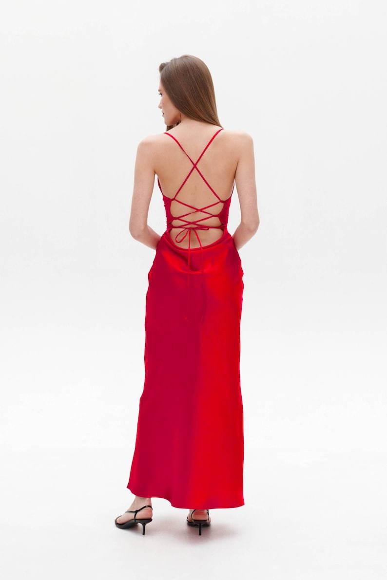 Puede incluir: Un vestido maxi de sat&eacute;n rojo con la espalda atada en forma de cruz.