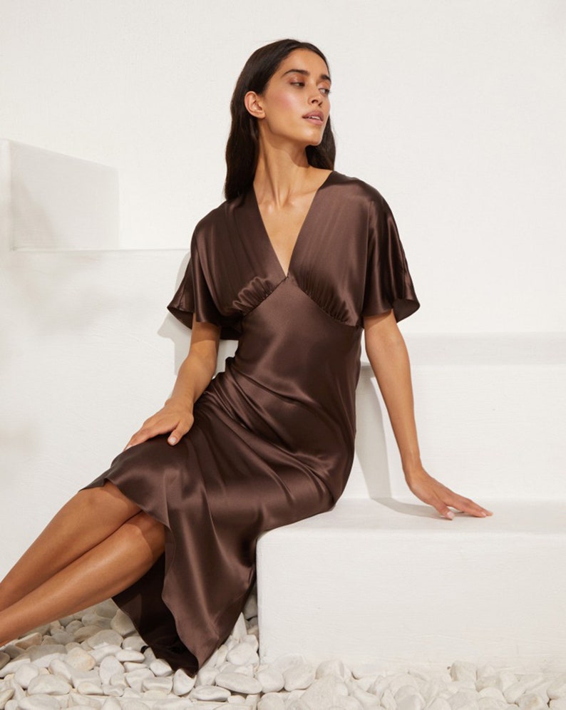 May include: A brown silk midi dress with a V-neckline and short, flared sleeves. The dress is fitted through the bodice and flows loosely from the waist.