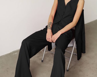 May include: A woman wearing a black sleeveless top and wide-leg pants sits on a metal chair. She is wearing black sunglasses and has a tattoo on her arm.