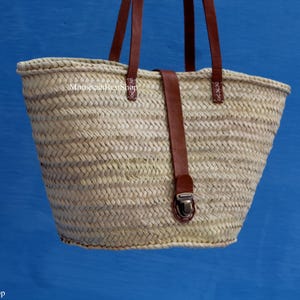 Handwoven Moroccan straw bag with long leather handles and a central leather buckle closure, lightweight boho-style tote perfect for summer or travel.