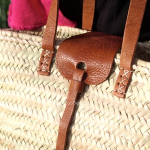 May include: A close-up of a woven straw tote bag with brown leather straps and a leather handle. The straps are stitched with white thread.