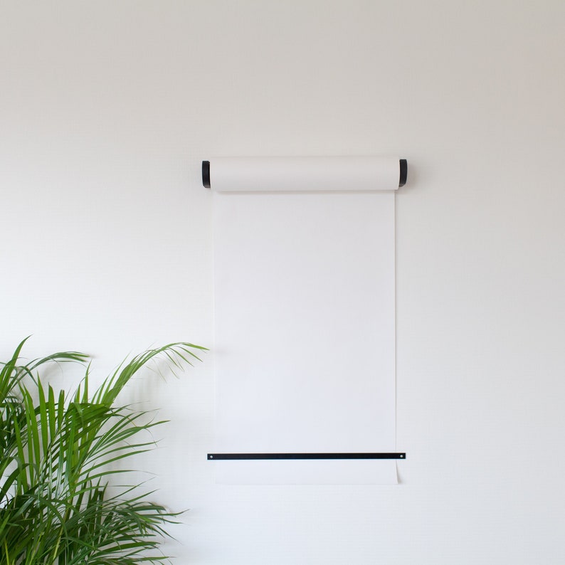 May include: A white roll of paper mounted on a white wall with black metal brackets. The paper is rolled up at the top and has a black metal bar at the bottom.