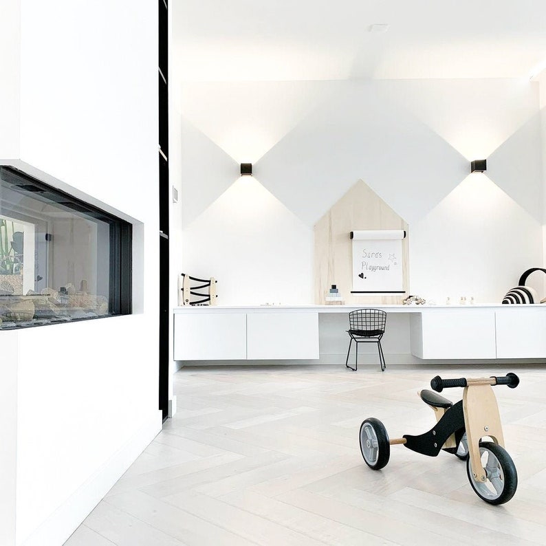 May include: A white room with a black and wood balance bike, a white desk with a black chair, and a white wall with a wooden triangle and a white board that says "Soren's Playground".