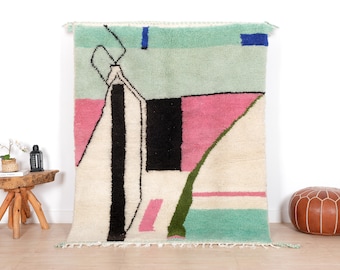 May include: An abstract rug with a geometric design in cream, black, pink, green, blue, and mint green. The rug has a fringe along the bottom edge. The rug's design is reminiscent of modern art.