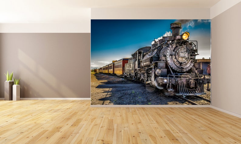 May include: A vintage steam locomotive train with a black engine and red and yellow passenger cars. The train is moving forward on a track with a blue sky and white clouds in the background.