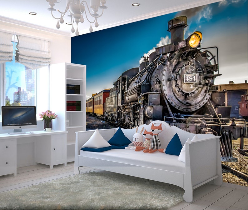 May include: A white daybed with blue and white pillows in front of a wall mural featuring a vintage steam locomotive with the number 484 on the side. The train is emitting smoke and has a bright yellow headlight.