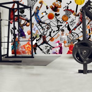 A gym interior with a wall mural featuring a basketball theme. The mural is a collage of basketball players in various poses, basketballs, and basketball hoops. The gym also has a weight bench, dumbbells, a kettlebell, and a blue exercise ball.