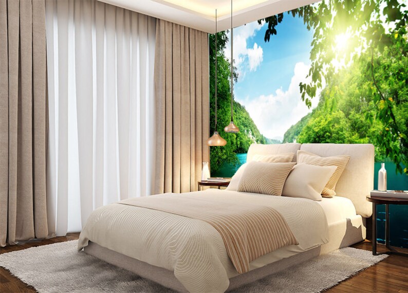 May include: A bedroom featuring a large wall mural depicting a verdant landscape with a river and mountains. The bed is dressed with beige linens and pillows. The room has beige curtains and a white rug.