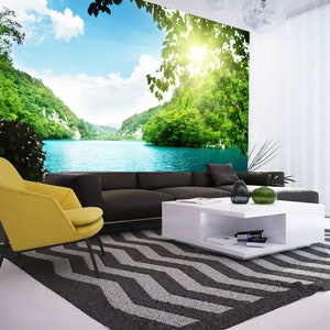 May include: A living room interior design featuring a large wall mural depicting a scenic lake surrounded by lush green trees and a bright blue sky. The room includes a yellow armchair, a black sofa, a white coffee table, and a black and white patterned rug.