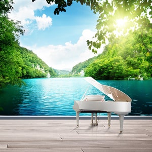 May include: A white grand piano with the lid open sits in front of a scenic landscape. The background features a lake surrounded by lush green trees and a bright blue sky with white clouds.
