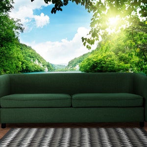 May include: A dark green sofa with a curved back sits in front of a wall mural depicting a lush green forest and a lake with a bright blue sky and white clouds.