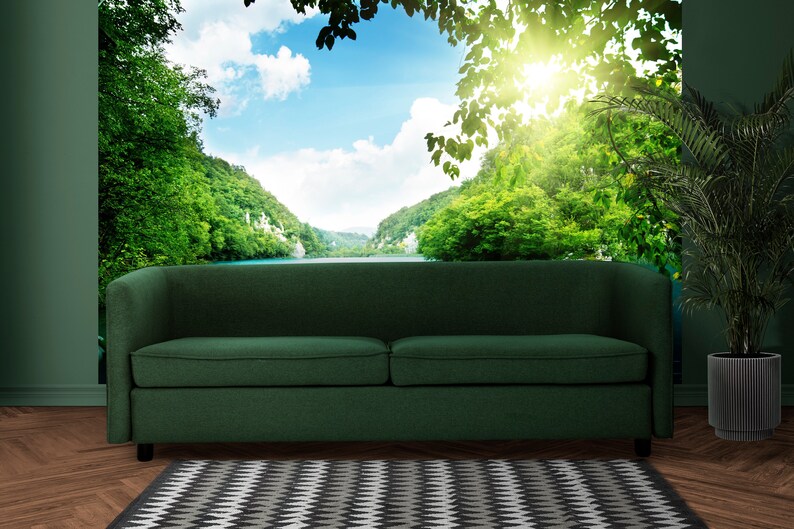 May include: A dark green sofa with a curved back sits in front of a wall mural depicting a lush green forest and a lake with a bright blue sky and white clouds.