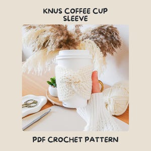 Pode incluir: Uma manga para copo de café branca com um design de malha torcida e texturizada. O texto KNUS COFFEE CUP SLEEVE e PDF CROCHET PATTERN está impresso a preto no topo e na base da imagem, emoldurando o artigo de crochet central.