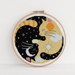 Puede incluir: Un diseño de gato negro y naranja bordado en punto de cruz en un aro de madera para bordar. El gato está enroscado en forma de yin-yang, con un lado que representa la noche y el otro el día.