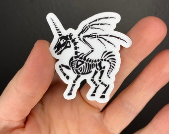 May include: Black and white sticker of a skeleton unicorn with wings. The unicorn is standing on all four legs and has a horn on its head.