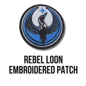 May include: Embroidered patch featuring a stylized black bird with outstretched wings, a red eye, and a star. The bird is set against a blue and white circular background. The text "REBEL LOON EMBROIDERED PATCH" is below the patch.
