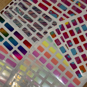 May include: Multiple sheets of rectangular nail polish stickers featuring a variety of finishes including holographic gradients, marbled patterns, solid neon colors, and metallic gold foil designs arranged in a grid layout on white backing paper.