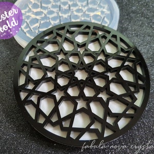 Può includere: Sottobicchiere nero con un motivo geometrico a stella. Il sottobicchiere è rotondo e presenta un design traforato. Le parole "Coaster Mold" sono nell'angolo in alto a sinistra. Le parole "fabula nova crystallis" sono in basso a destra.