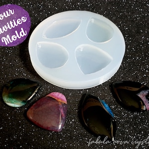 May include: A clear silicone mold with four cavities shaped like teardrop pendants. The mold is on a black sparkly surface. Four teardrop pendants made with resin are next to the mold.
