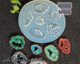 May include: A silicone mold for making geode-shaped resin crafts. The mold has six cavities, each shaped like a geode with a crystal-like pattern. The mold is light blue and is sitting on a black surface. There are also six finished geode-shaped resin pieces in various colors, including green, blue, red, and white.