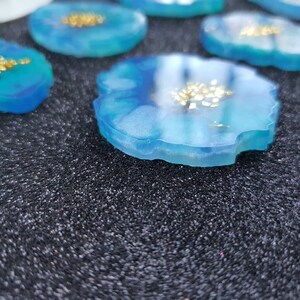 May include: Close-up of a blue resin coaster with gold flecks. The coaster has an irregular, agate-like shape.