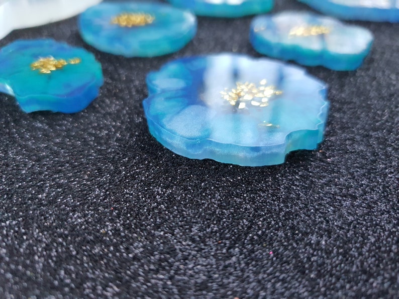May include: Close-up of a blue resin coaster with gold flecks. The coaster has an irregular, agate-like shape.