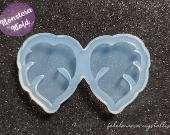 May include: A light blue silicone mold in the shape of two connected leaves. The mold has a smooth surface and is designed for crafting. The text "Monstera Mold" is in a purple circle. The text "fabula nova crystallis" is at the bottom.