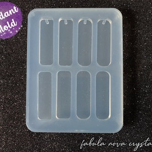 May include: A clear silicone mold with six rectangular cavities for making pendant jewelry. Each cavity has a small hole at the top for adding a jump ring.