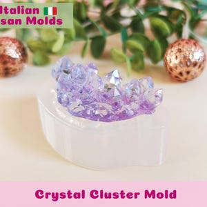 May include: A light purple crystal cluster mold on a white, curved base. The mold is surrounded by two decorative bronze spheres and greenery. The text "Crystal Cluster Mold" is at the bottom.