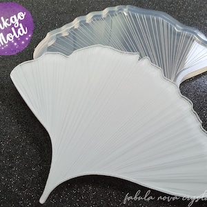 Può includere: Uno stampo trasparente a forma di foglia di ginkgo per l'artigianato. Lo stampo è realizzato in un materiale traslucido e presenta dettagliate linee di venature. Il testo "Ginkgo Mold" è in un cerchio viola e il testo "fabula nova crystallis" è in basso.