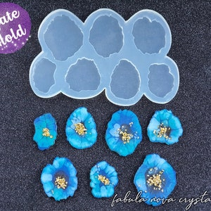 May include: A silicone mold shaped like a cloud with six agate-shaped cavities. The mold is shown with six finished resin pieces that resemble blue agate with gold flecks. The text "Agate Mold" is written in purple on a sparkly purple background. The text "fabula nova crystallis" is written in white on a black background.