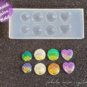 Puede incluir: Un molde de silicona transparente con seis cavidades redondas y dos en forma de corazón. El molde está diseñado para crear formas de escamas de sirena. La imagen también muestra varias formas de escamas de sirena iridiscentes hechas con el molde.