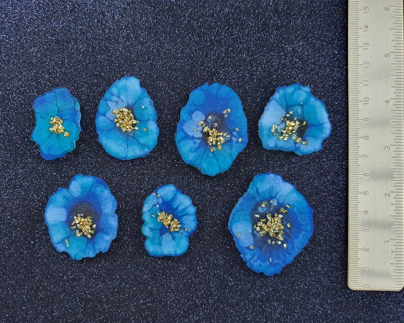 May include: Seven blue resin flower embellishments with gold glitter accents. The flowers are approximately 1 inch in diameter.