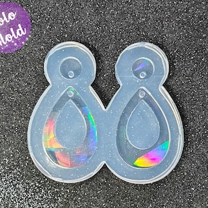 Pode incluir: Molde de silicone transparente para fazer dois brincos em forma de lágrima com um pequeno furo no topo de cada brinco.